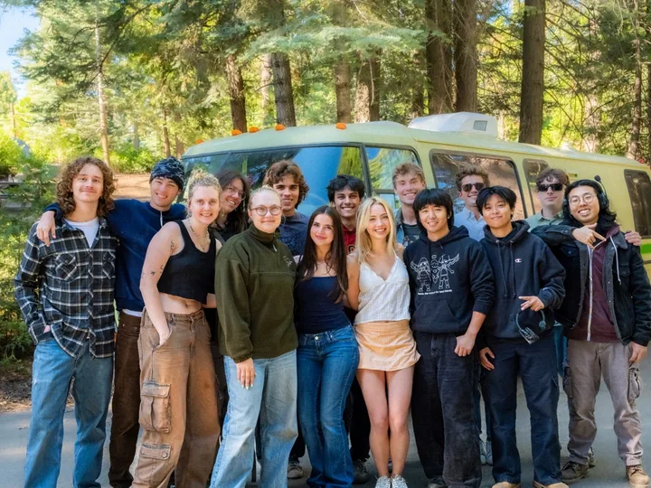 The cast and crew standing together beside the green RV among tall trees